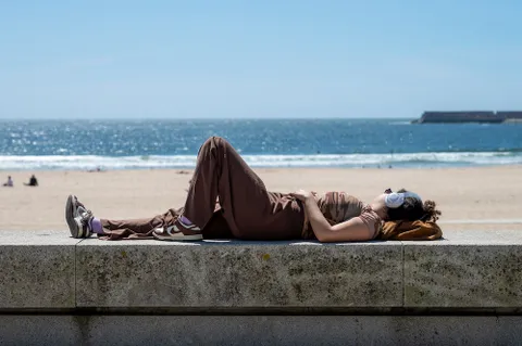 Young woman wearing headphones while laying near the beach