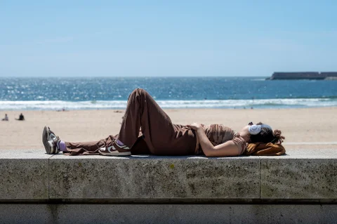Young woman wearing headphones while laying near the beach