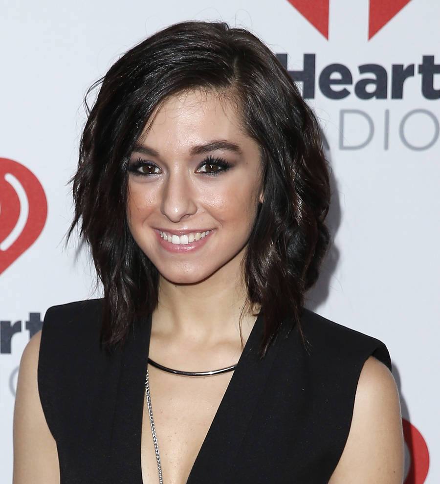 Christina Grimmie at a concert, singing into a microphone with her eyes closed, wearing a black top