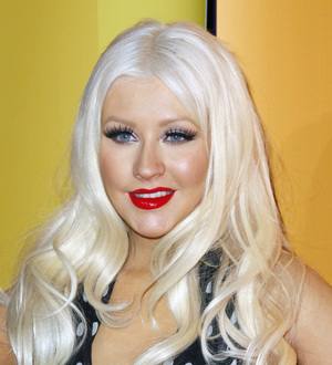 Christina Aguilera in a black dress performs on stage with a microphone
