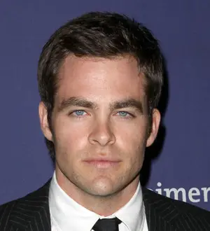 Chris Pine in a gray t-shirt and white shorts, looking at a phone while walking outdoors
