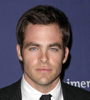 Chris Pine in a gray t-shirt and white shorts, looking at a phone while walking outdoors