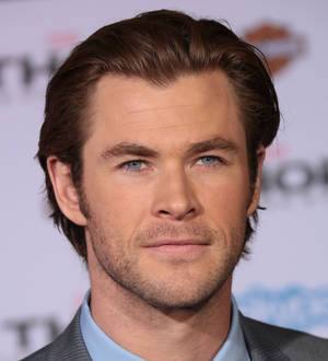 Chris Hemsworth in a distressed t-shirt in a speedboat on a flooded street surrounded by debris