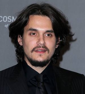 John Mayer performing on stage, playing an acoustic guitar and singing into a microphone