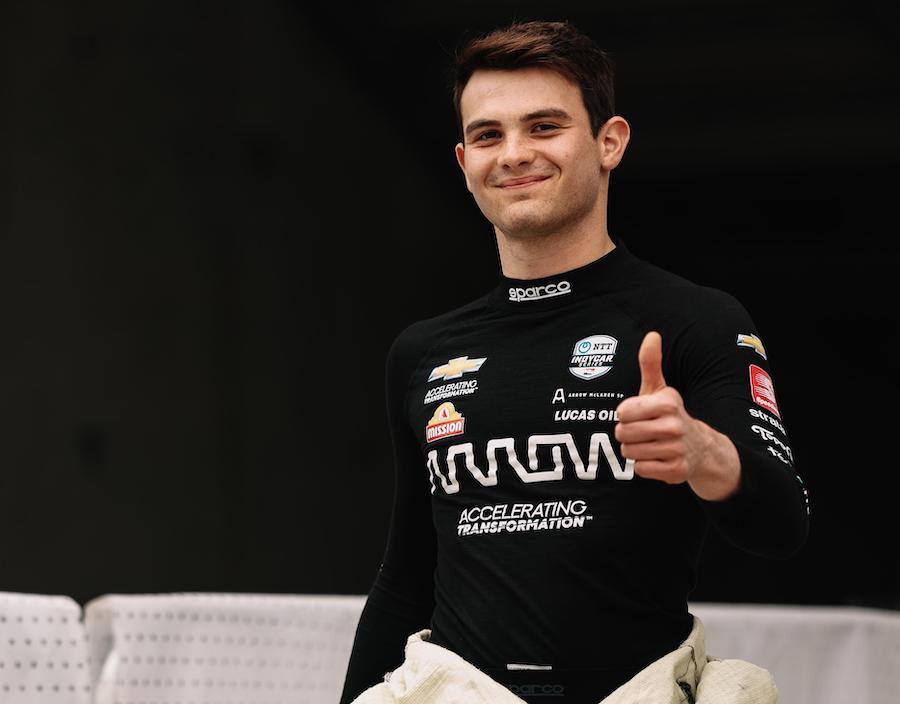 Pato O'Ward smiles from a race car cockpit in his firesuit and helmet