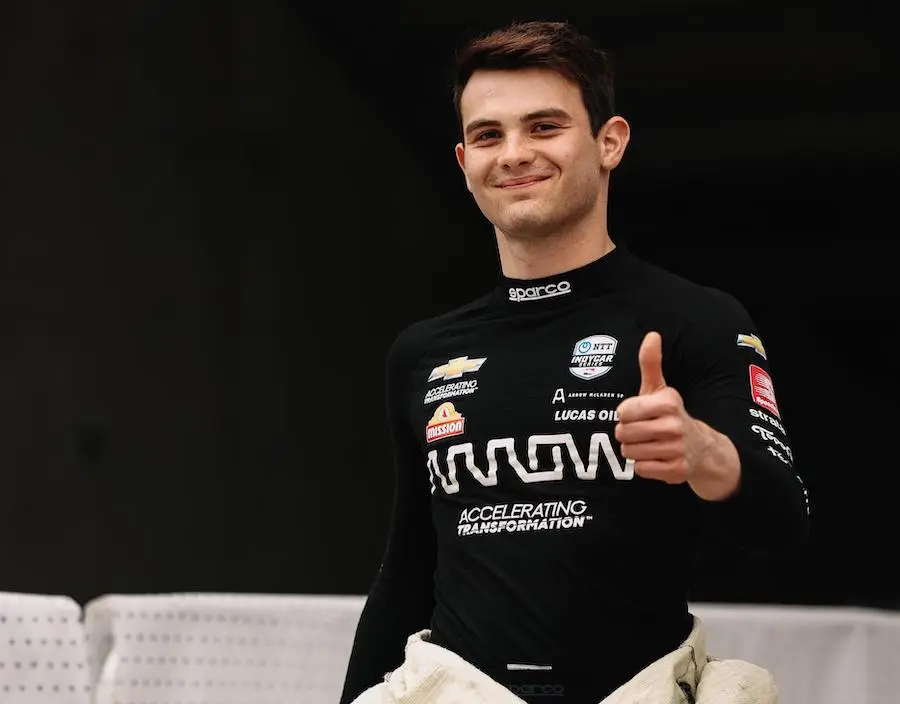 Pato O'Ward smiles from a race car cockpit in his firesuit and helmet