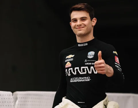Pato O'Ward smiles from a race car cockpit in his firesuit and helmet
