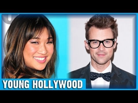 Jenna Ushkowitz in an elegant black dress, styled by Brad Goreski, stands in a brightly lit room