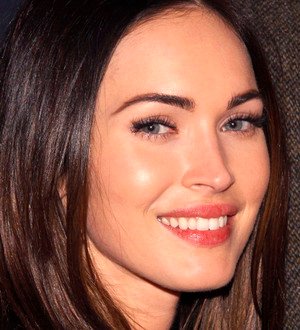 Megan Fox on a red carpet, smiling while looking towards the camera