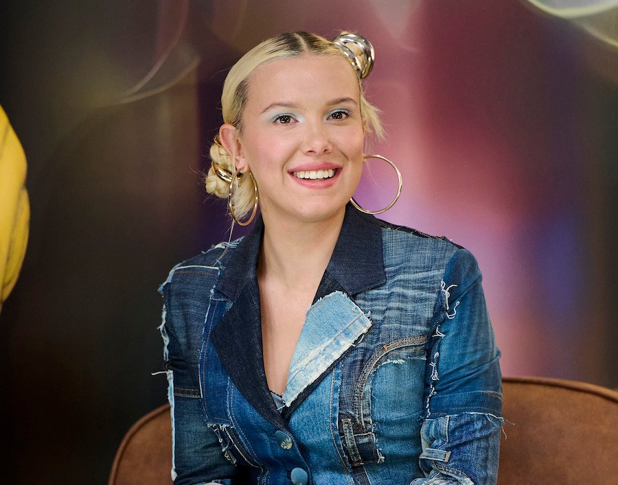 Millie Bobby Brown poses for a photo, wearing a pale blue top and bold jewelry