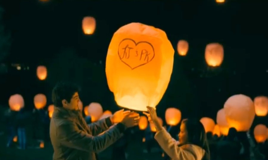 A couple holds hands while walking through a city park, with autumn leaves visible on the trees