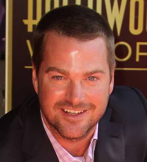 Chris O'Donnell in a blue suit and sunglasses, kneels next to his Hollywood Walk of Fame star on a sunny street
