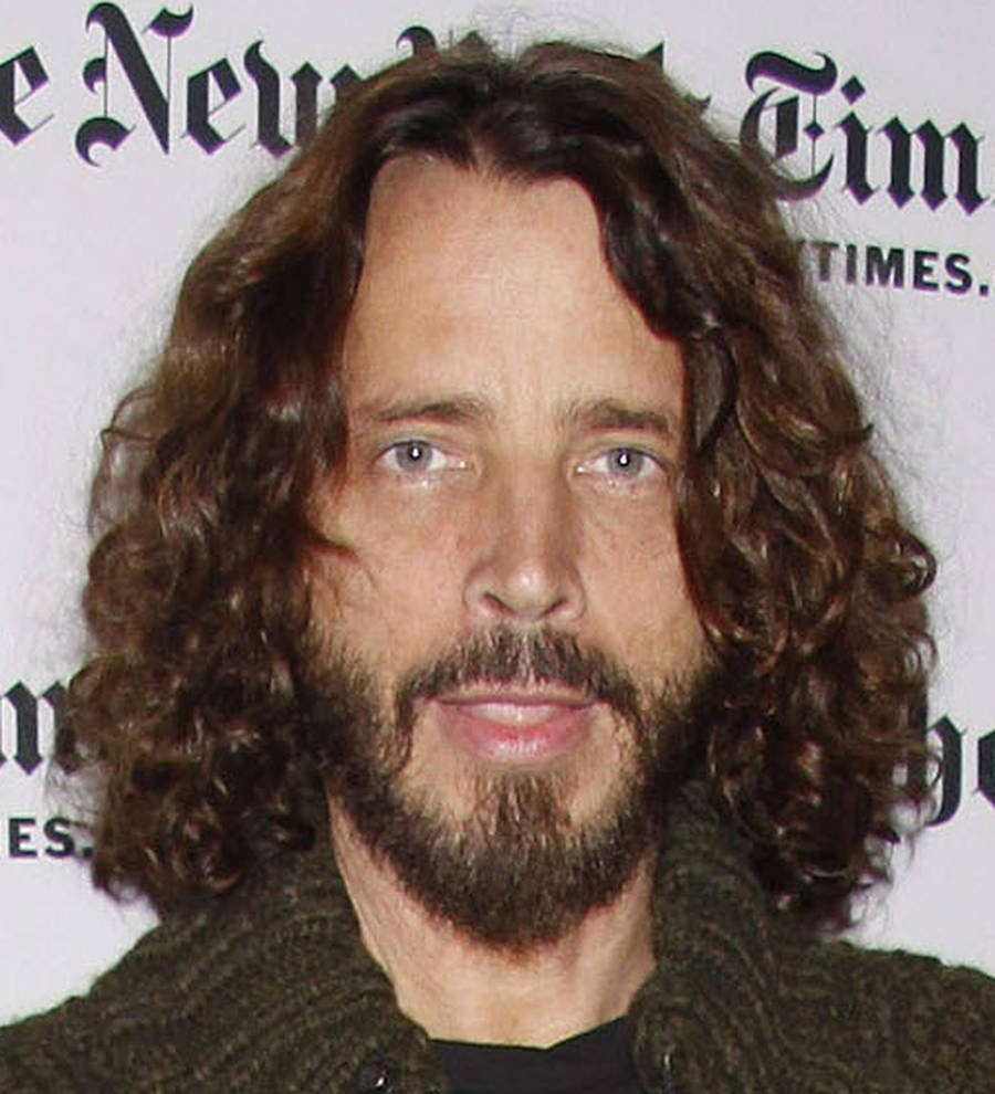 Chris Cornell in a black suit and shirt on a red carpet, smiling slightly