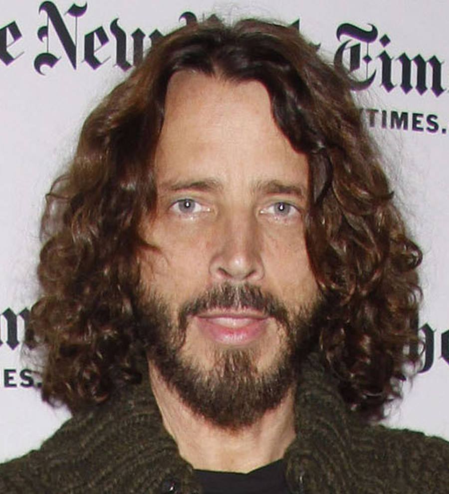 Chris Cornell in a black suit and shirt on a red carpet, smiling slightly