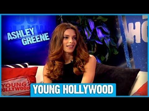 Ashley Greene facing the camera with a slight smile, posing in a dark top in a studio setting