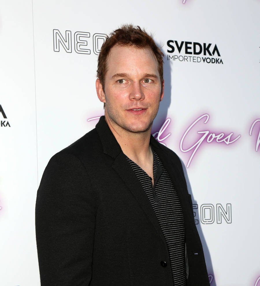 Chris Pratt looks seriously at the camera, wearing a dark blue suit and striped tie