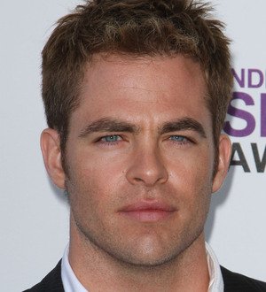 Chris Pine on a red carpet, head tilted as he smiles. He has a beard and blue eyes