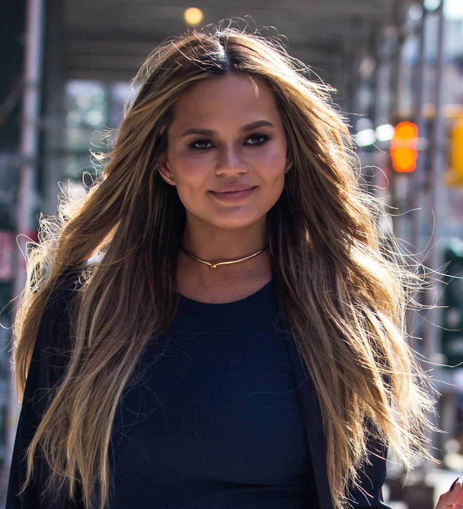 Chrissy Teigen in a black sequined dress and heels poses on a red carpet