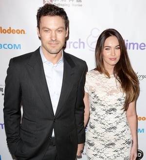 Megan Fox in a tight black tank top and dark pants smiles for a photo