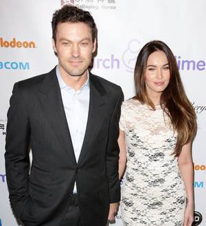 Megan Fox in a tight black tank top and dark pants smiles for a photo