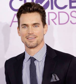 Matt Bomer smiles in a close-up photo, wearing a blue shirt and black jacket
