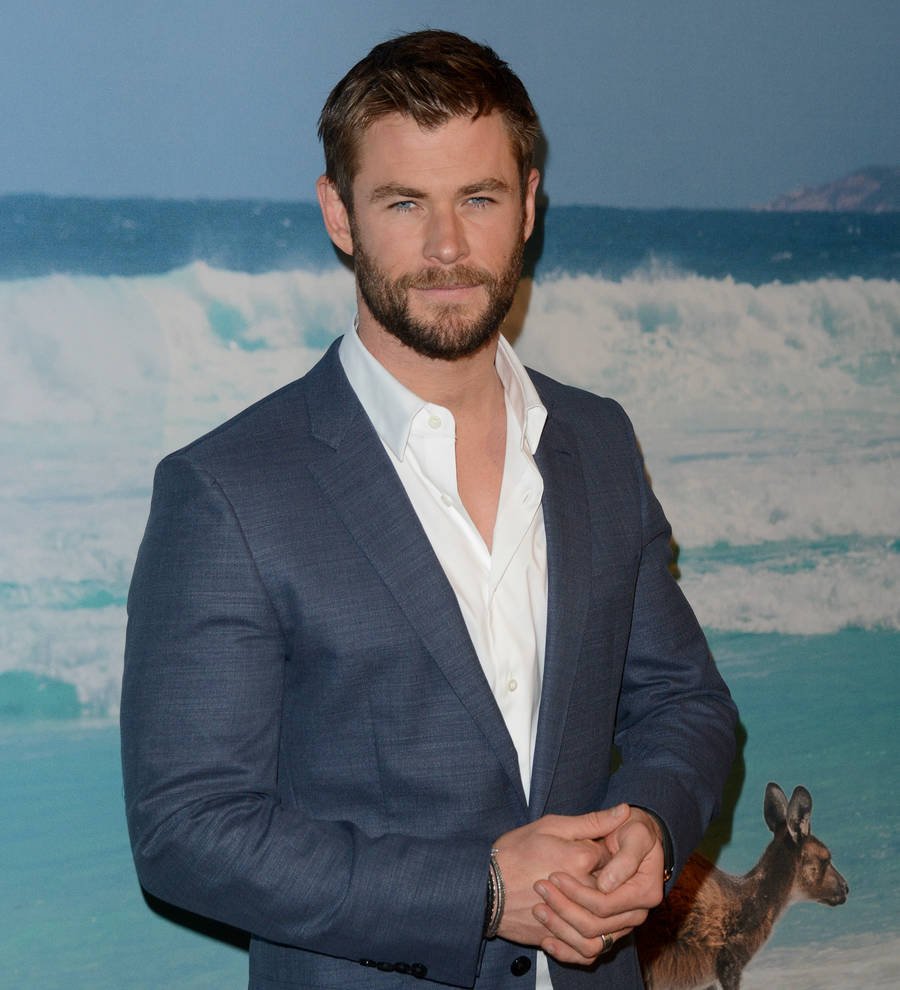 Chris Hemsworth in a gym, shirtless, flexing biceps in front of a mirror