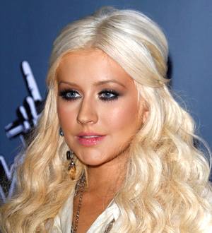 Christina Aguilera in a black off-the-shoulder dress poses with hands on her knees, white background