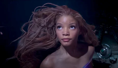 Halle Bailey as Ariel, a Black woman with long red braids, swimming underwater