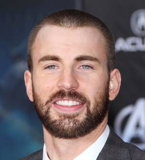 Chris Evans smiling, wearing a dark blue shirt and a multi-colored striped tie, posing indoors