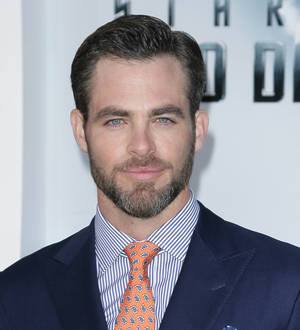 Chris Pine, wearing a black suit with his hands in pockets, faces the camera with a slight smile
