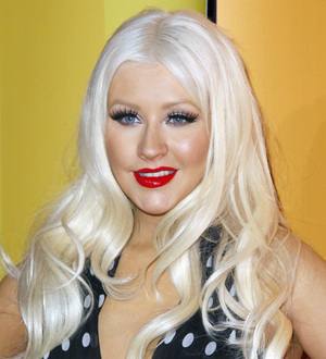 Christina Aguilera stands on a dimly lit stage, bathed in blue light, singing into a microphone