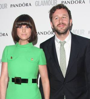 Chris O'Dowd standing outdoors, smiling and holding a small dog in his arms