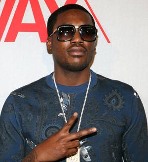 Meek Mill speaks at a podium in front of a blue backdrop, holding a small trophy