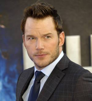 Chris Pratt smiling for the camera, wearing an ornate tan and black suit jacket with a bowtie