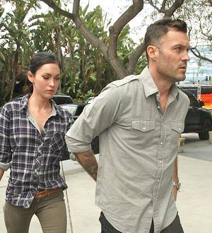 Megan Fox smiles, holding her newborn in a hospital bed, her partner looking on adoringly