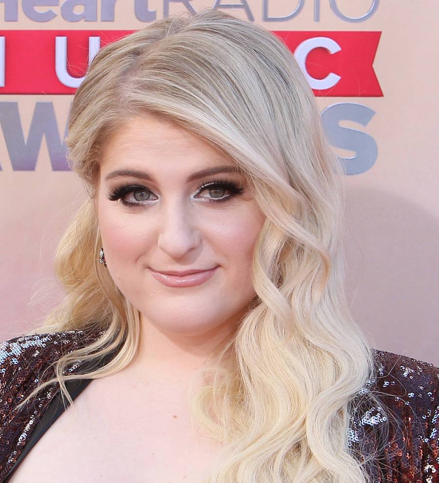 Meghan Trainor holding a microphone and singing on a stage, purple and blue lighting