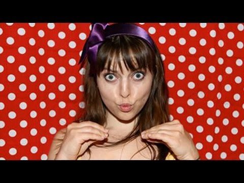 Olga Kay holds up a colorful digital camera, smiling broadly at the viewer