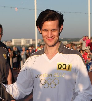 Matt Smith running in an Olympic torch relay, wearing a white tracksuit and holding a torch