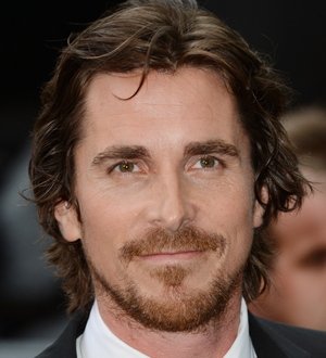 Christian Bale in a black t-shirt and jeans stands with a woman in a hospital gown