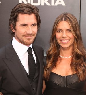 Christian Bale in a tuxedo and black bow tie, hands in pockets, on a red carpet
