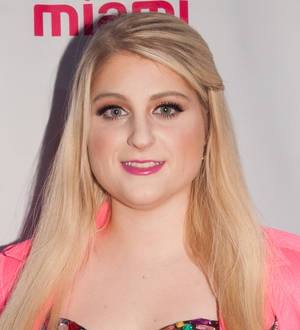 Meghan Trainor and Nick Jonas pose together on a red carpet, arms around each other's waists