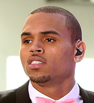 Chris Brown in a white shirt and sunglasses performs under blue stage lights