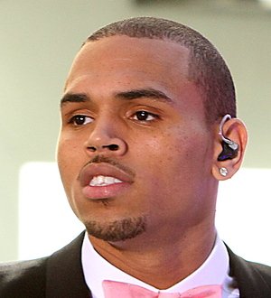 Chris Brown in a white shirt and sunglasses performs under blue stage lights