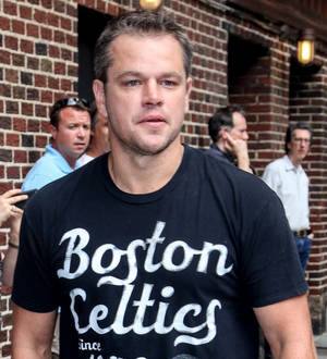 Matt Damon poses in a dark suit and white shirt, looking directly at the camera with a slight smile