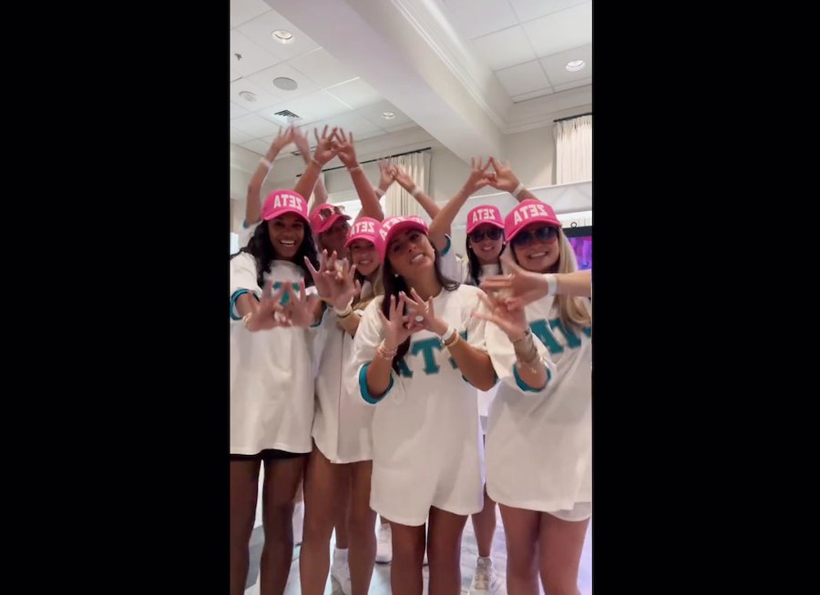 A group of women in formal dresses pose and smile at a sorority recruitment event