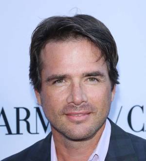Matthew Settle smiles in a blue shirt, hands behind his back