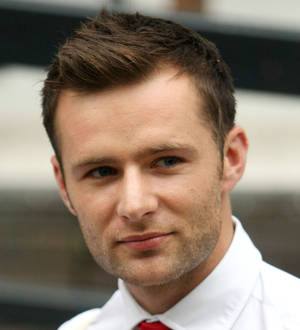 Harry Judd in a black suit smiles next to his bride in a white dress