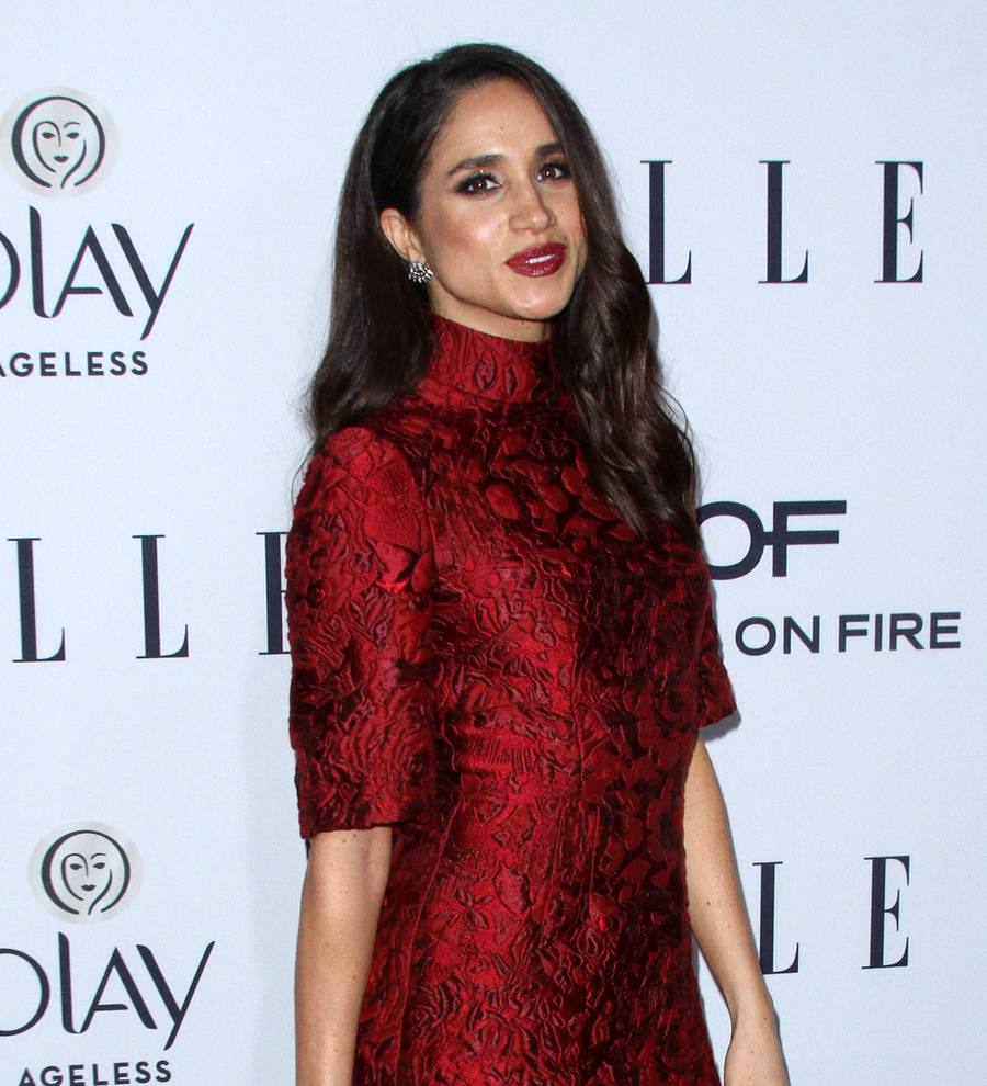 Meghan Markle on a dimly lit stage, looking to her left, wearing a white sleeveless top