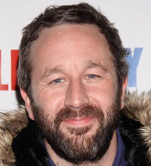 Chris O'Dowd with brown hair and beard speaks and gestures at a podium indoors