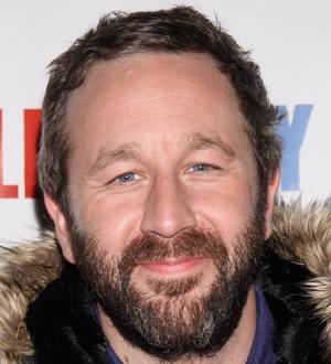 Chris O'Dowd with brown hair and beard speaks and gestures at a podium indoors